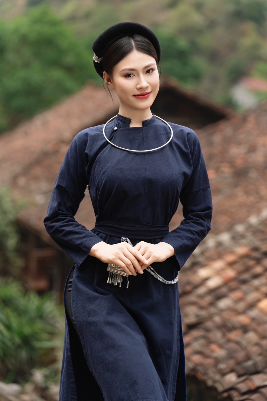 Thiếu nữ trong tà áo chàm và vòng bạc, phía sau là mái ngói âm dương